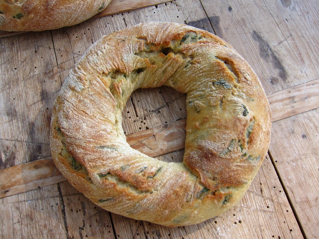 Ein rundes Brot mit einer krustigen Oberfläche und einem speziellen Muster, möglicherweise mit Kräutern oder anderen Zutaten.