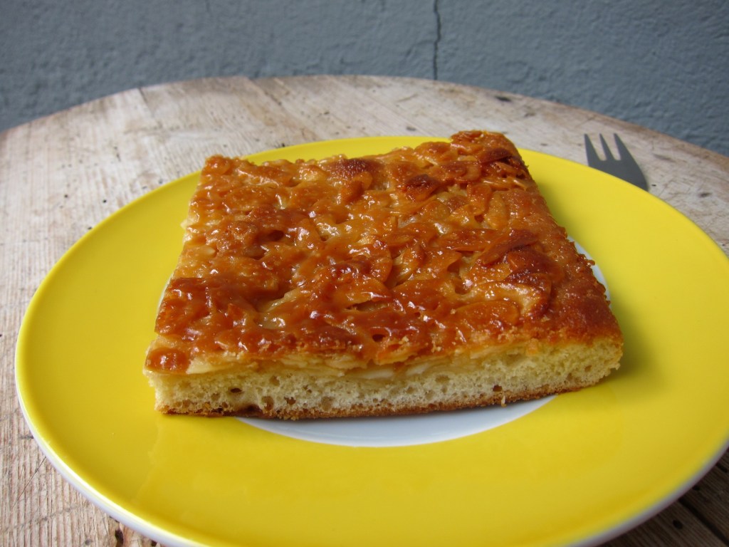 Ein Stück Butterkuchen auf einem gelben Teller, mit einer goldbraunen, karamellisierten Oberseite.