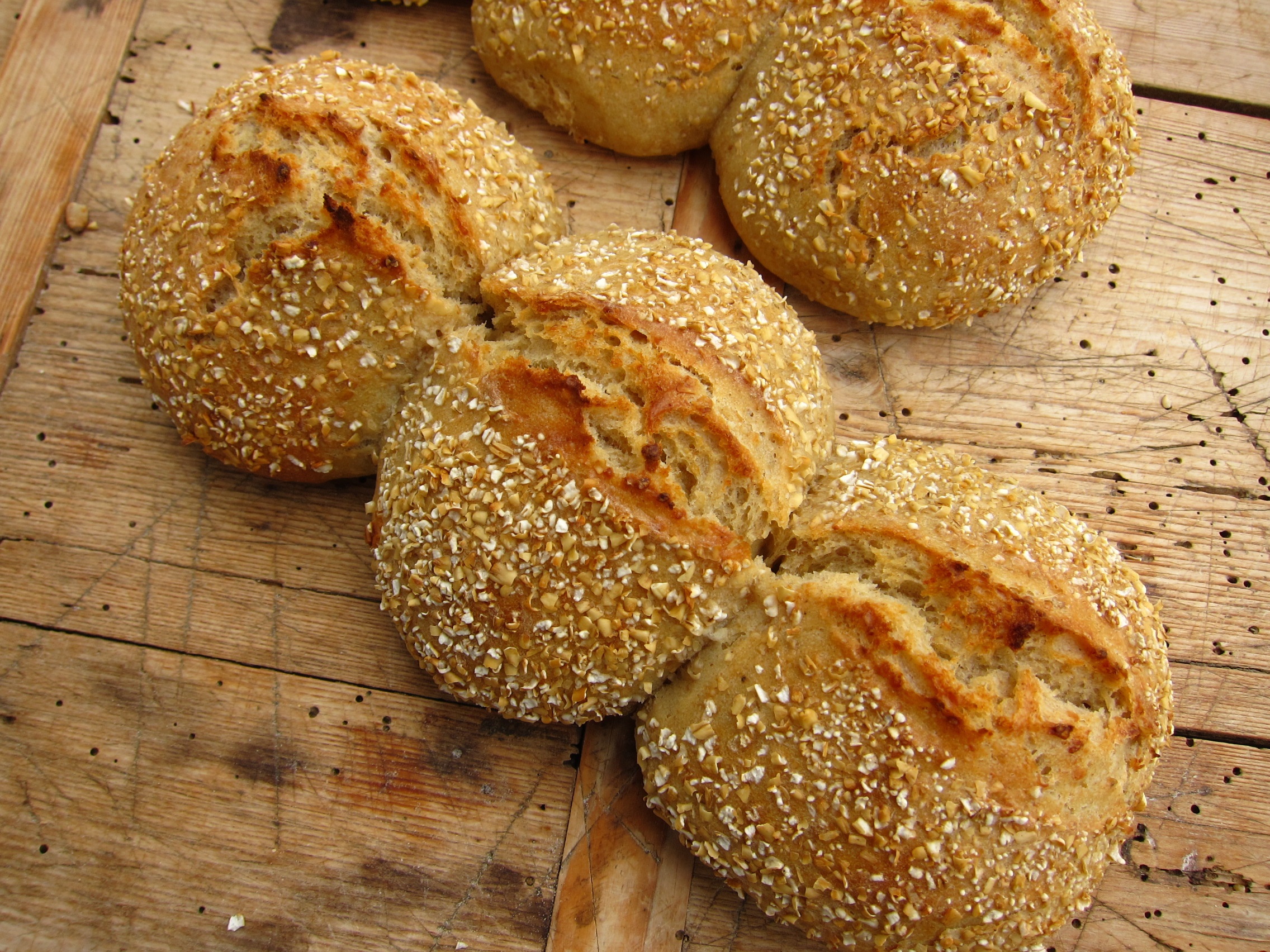 Brötchen mit Haferflocken überzogen, auf einem Holzbrett angeordnet.
