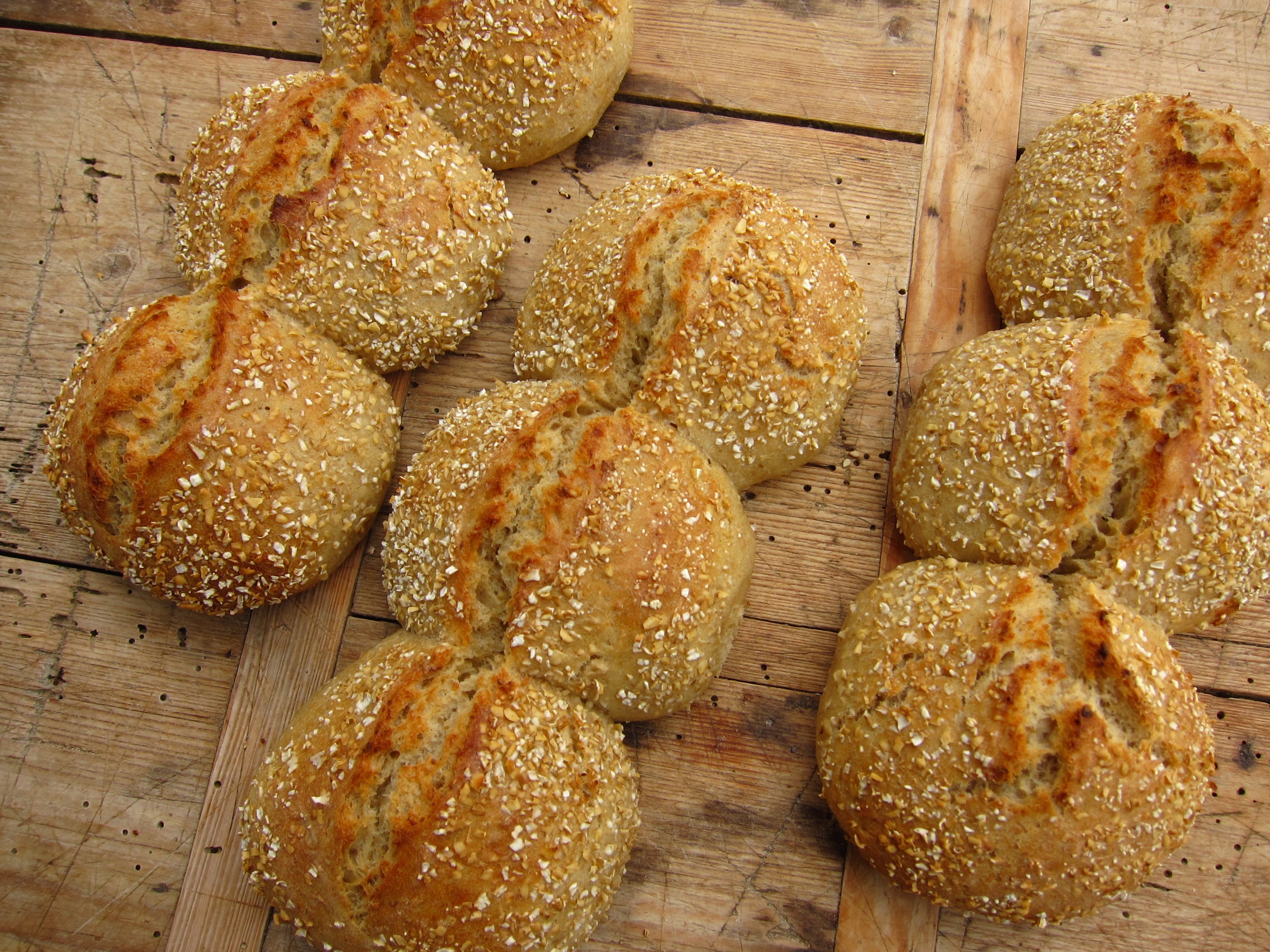 Mehrkornbrötchen mit einer goldenen, knusprigen Kruste und Haferflocken bestreut, auf einem Holztisch arrangiert.