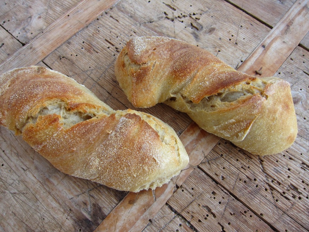Zwei frisch gebackene Ciabatta-Brote aus Weizenmehl auf einem Holzbrett.