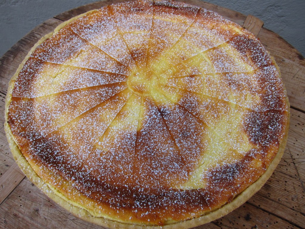 Ein flacher Käsekuchen mit goldbrauner Oberfläche und Puderzucker bestäubt.