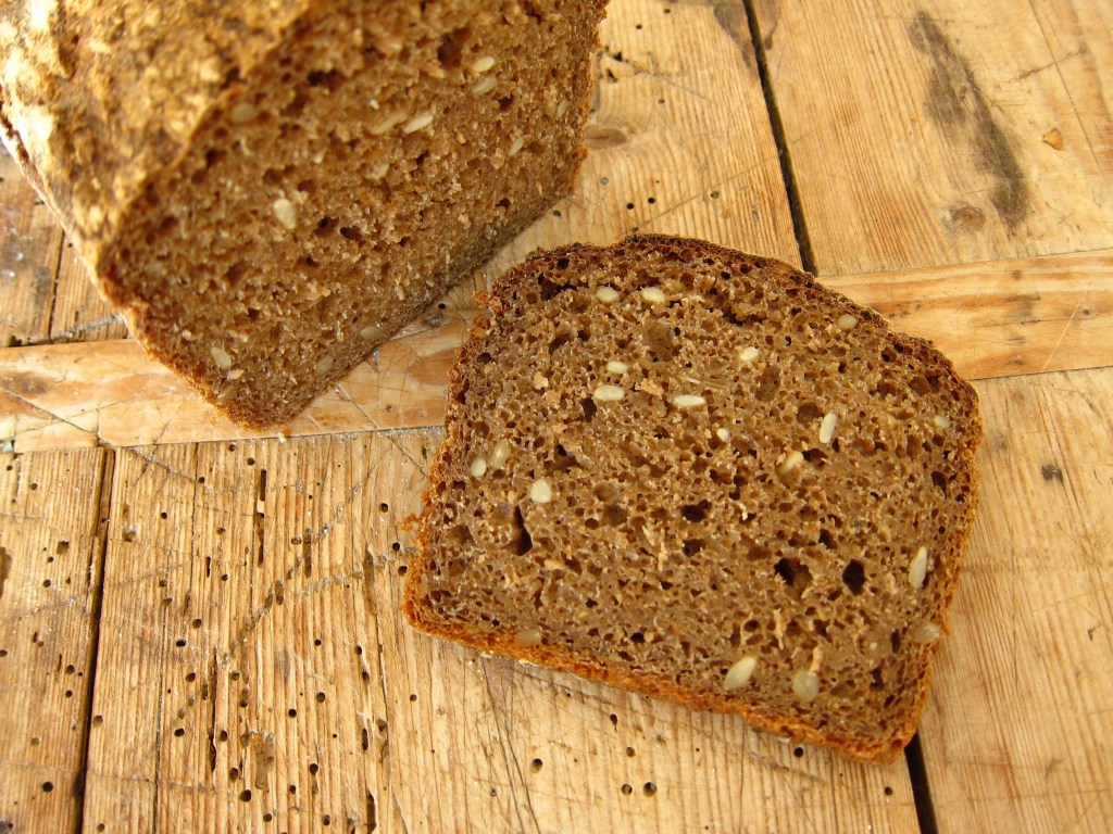 Ein Stück Roggenvollkornbrot mit einer dichten Krume und einer rustikalen Kruste, auf einem Holzbrett geschnitten.