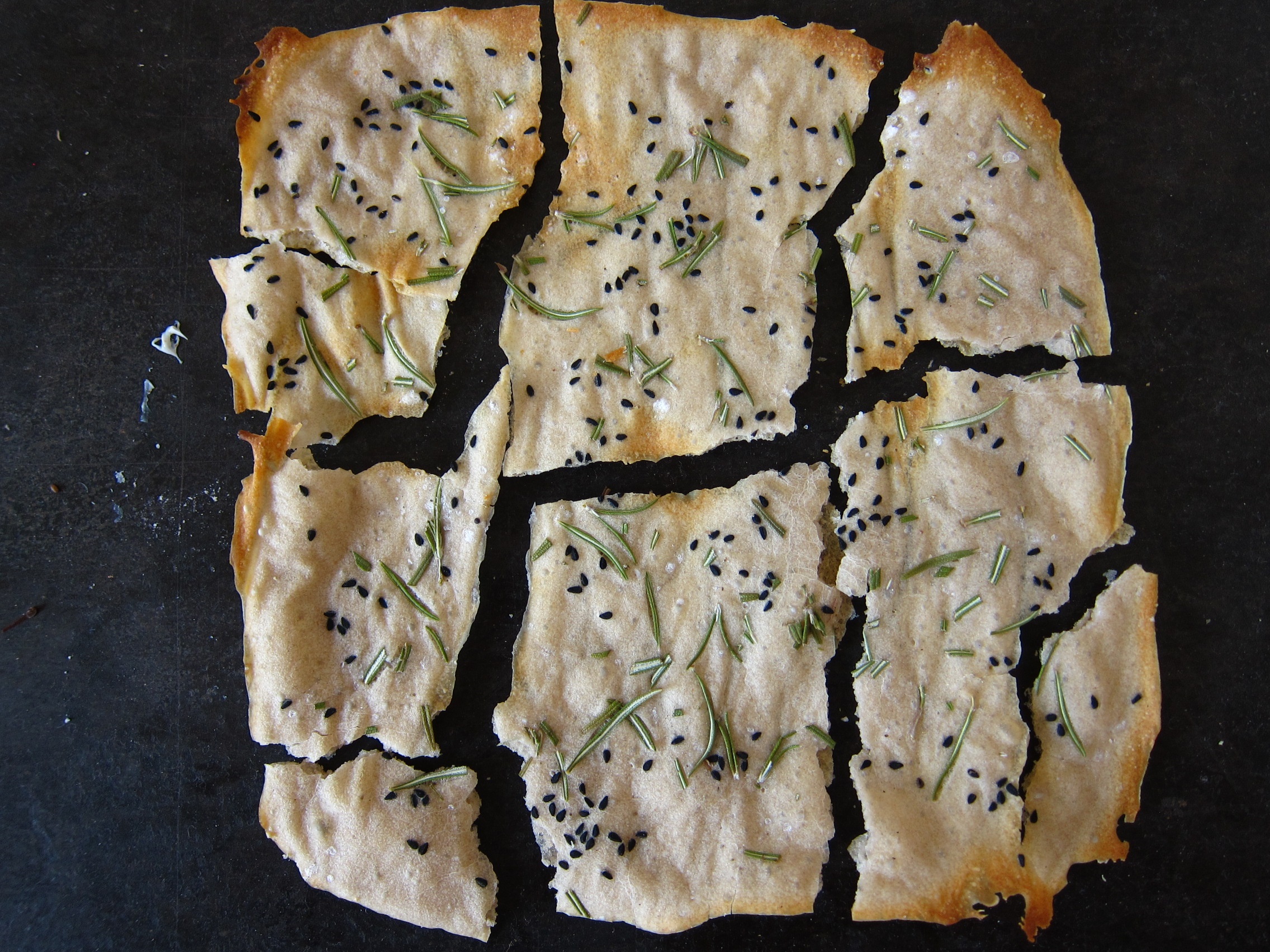 Ein zerbrochener Fladen aus Dinkelteig, gewürzt mit schwarzen Samen und Rosmarin.