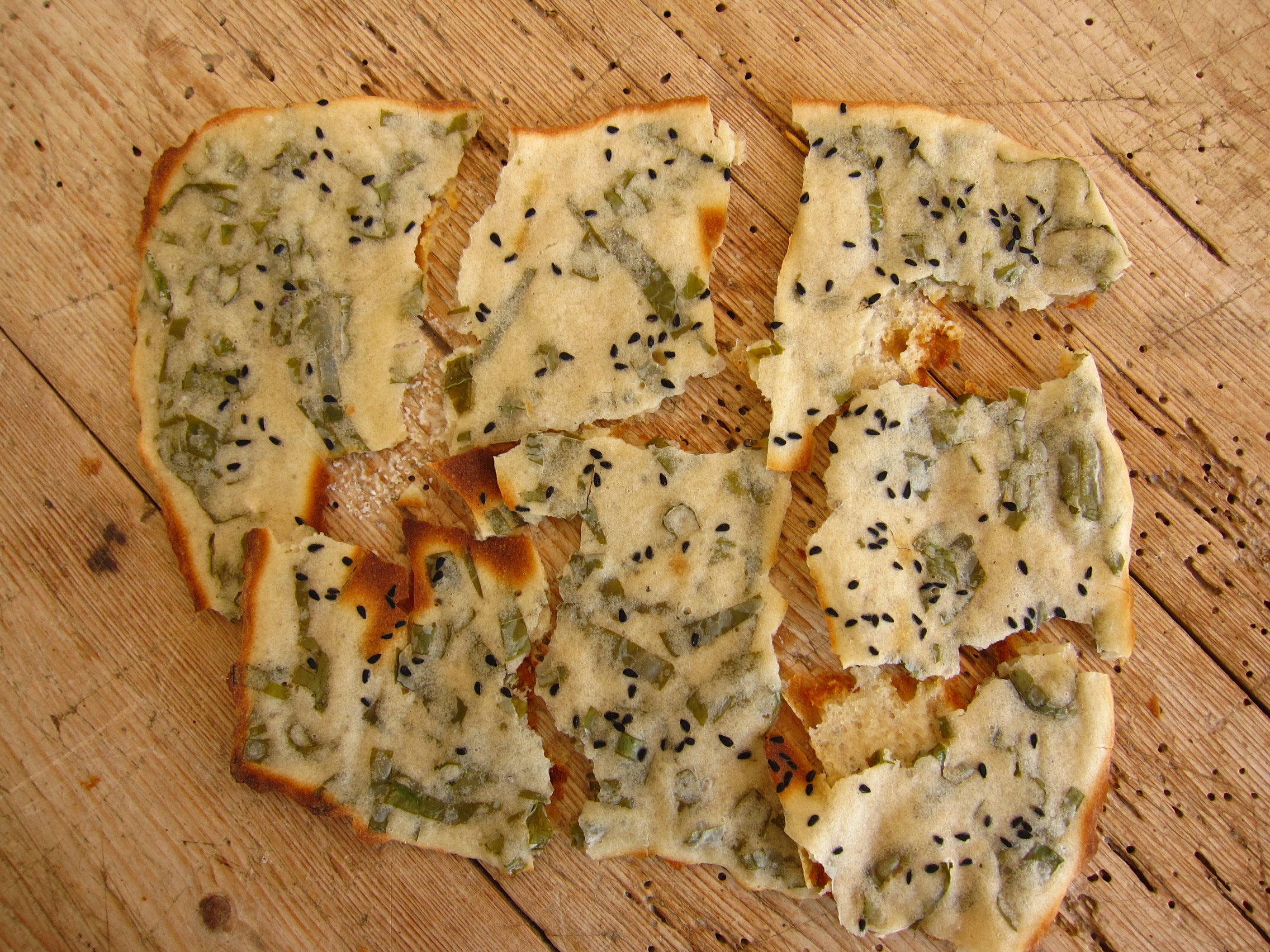 Fladenbrot mit grünen Zwiebeln und schwarzem Sesam, auf einem Holzbrett serviert.