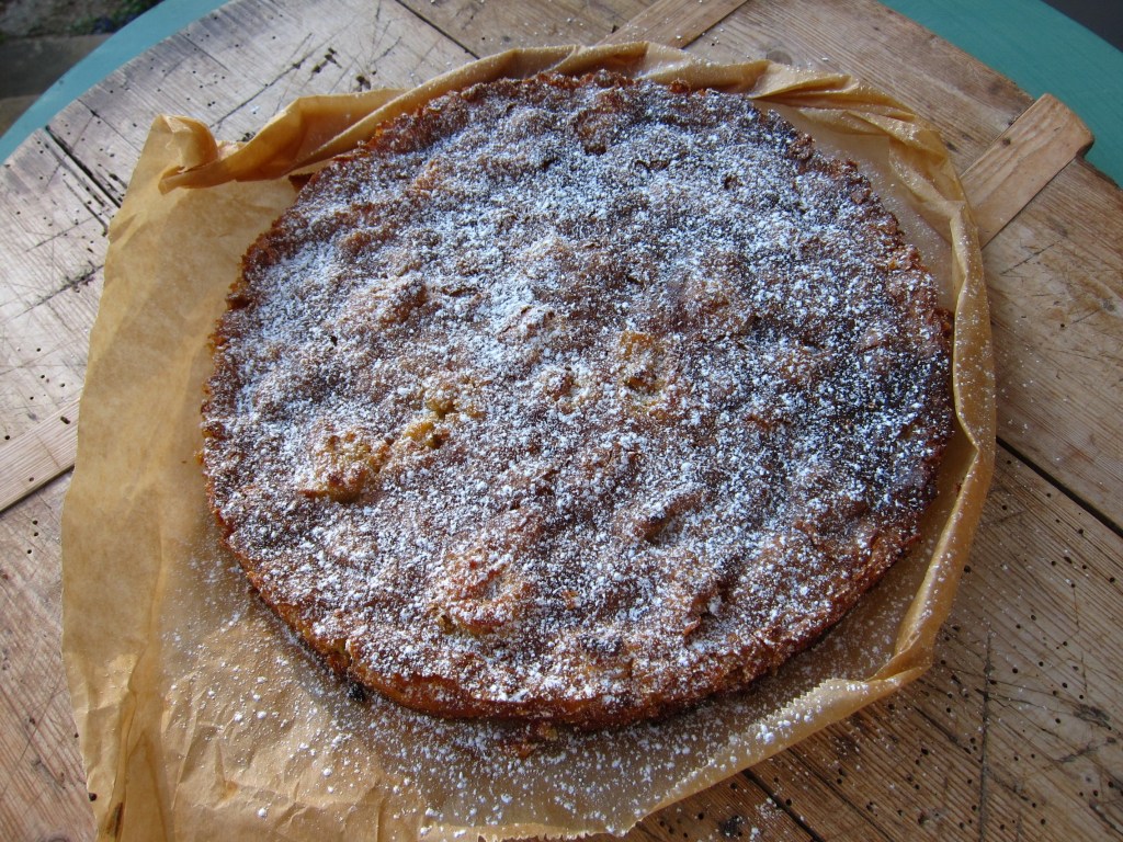 Ein gebackener Kuchen mit einer goldbraunen Oberfläche, bestäubt mit Puderzucker, auf einem Stück Backpapier.