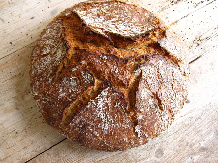 Ein frisch gebackenes rustikales Brot mit einer knusprigen Kruste auf einer Holzarbeitsfläche.