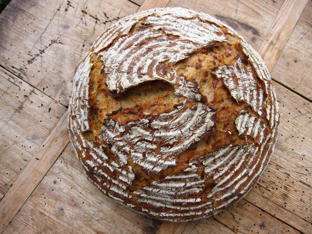 Ein runder Laib Brot mit einer knusprigen, rissigen Kruste, die gut gebräunt ist und eine weiche, luftige Innenseite besitzt.