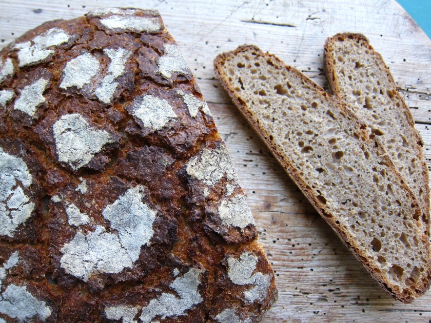 Ein rustikales Brot mit einer dunklen, knusprigen Kruste und mehreren Scheiben, die auf einem Holzbrett liegen.