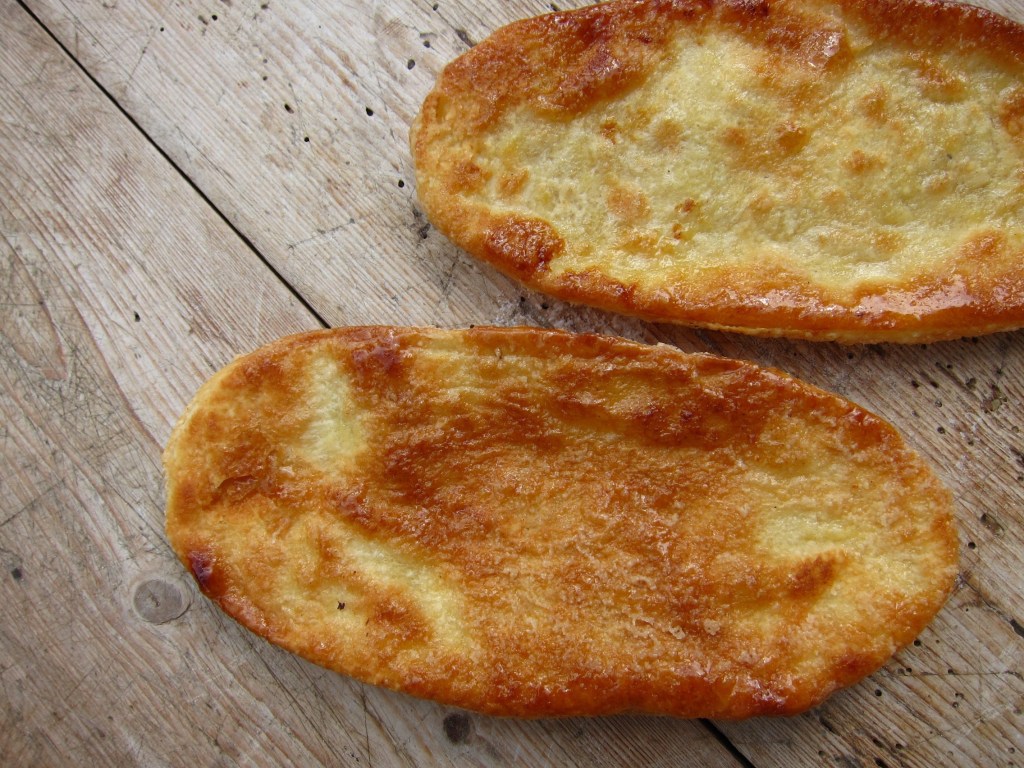 Zwei frisch gebackene Fladenbrote auf einer Holzoberfläche, knusprig und goldbraun.