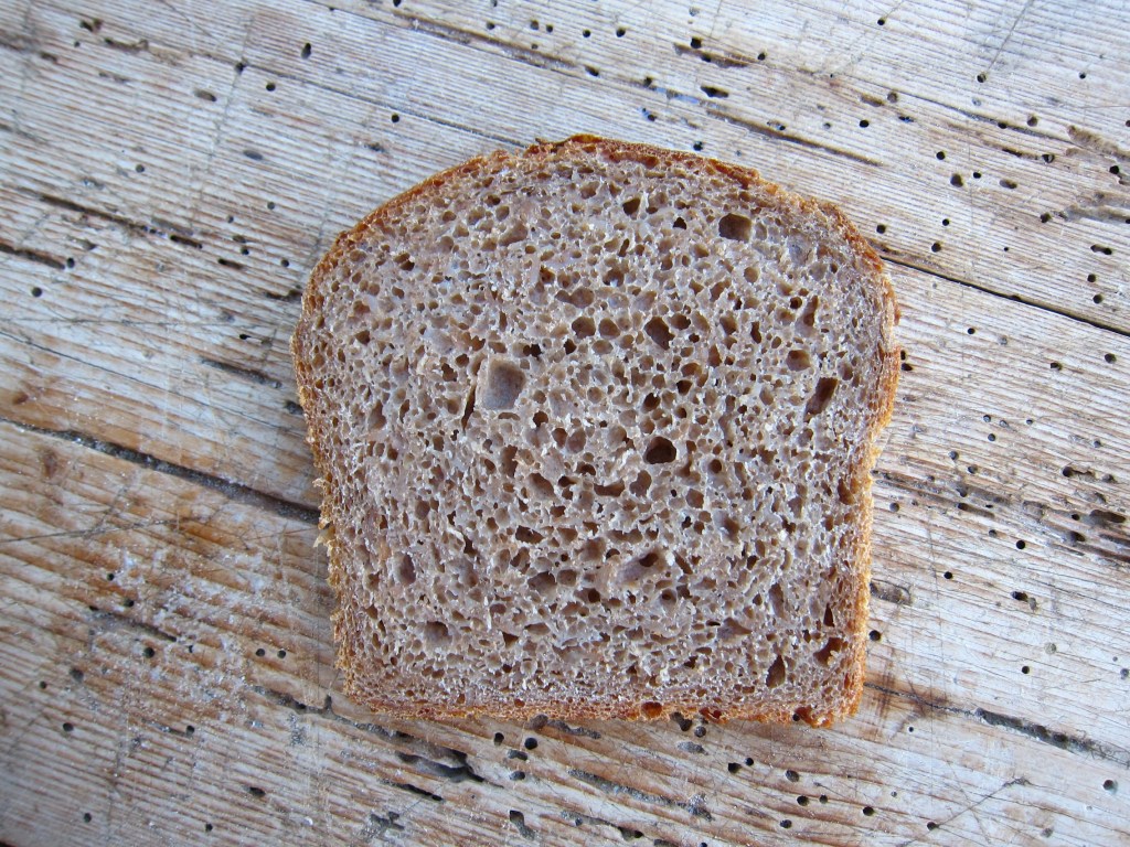 Ein aufgeschnittener Laib Vollkornbrot mit grober Krume und hellbrauner Rinde auf einem rustikalen Holztisch.