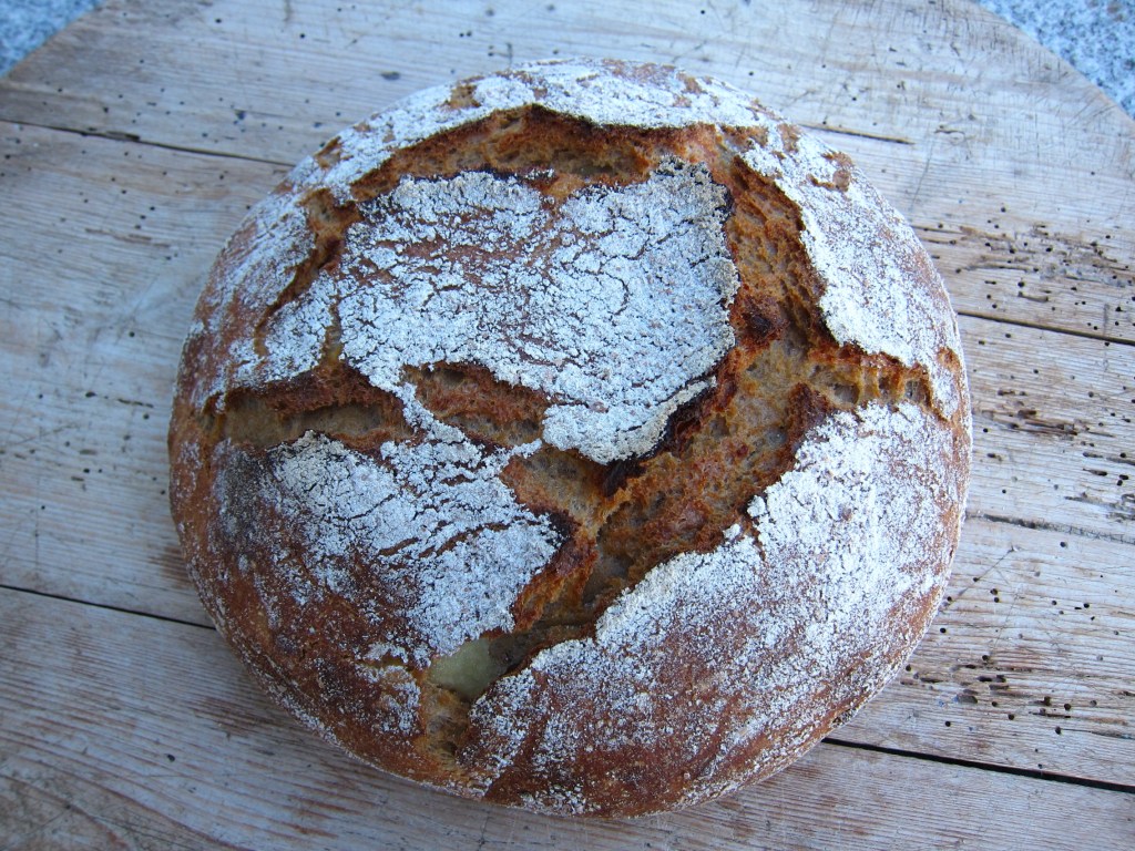 Ein rustikales Brot mit einer knusprigen Kruste und Rissen auf der Oberseite, auf einem Holzbrett platziert.