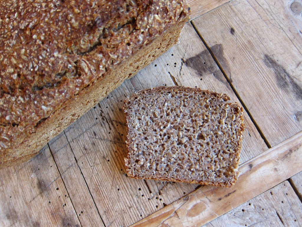Ein Laib vollkornbrot auf einem Holzbrett mit einer Scheibe daneben.