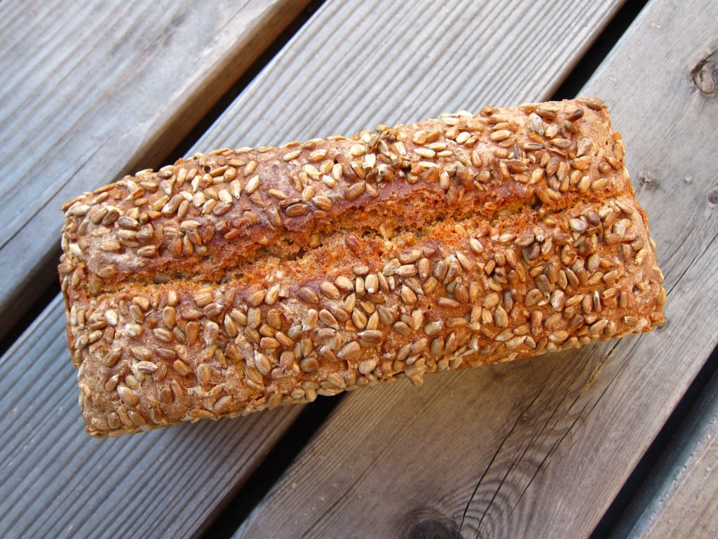 Ein Laib Brot mit einer knusprigen Kruste und großzügigem Sesam-Belag, auf einem Holztisch platziert.