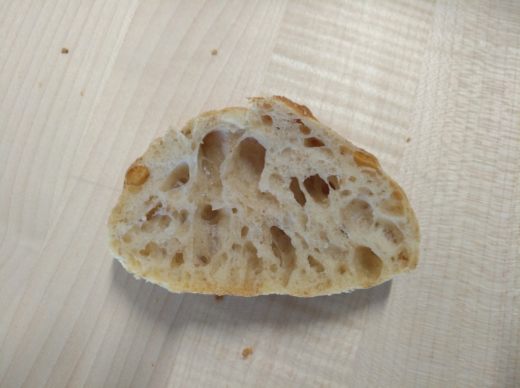 Aufgeschnittenes Brot mit luftiger, unregelmäßiger Krume und goldener Kruste auf einem Holzbrett.