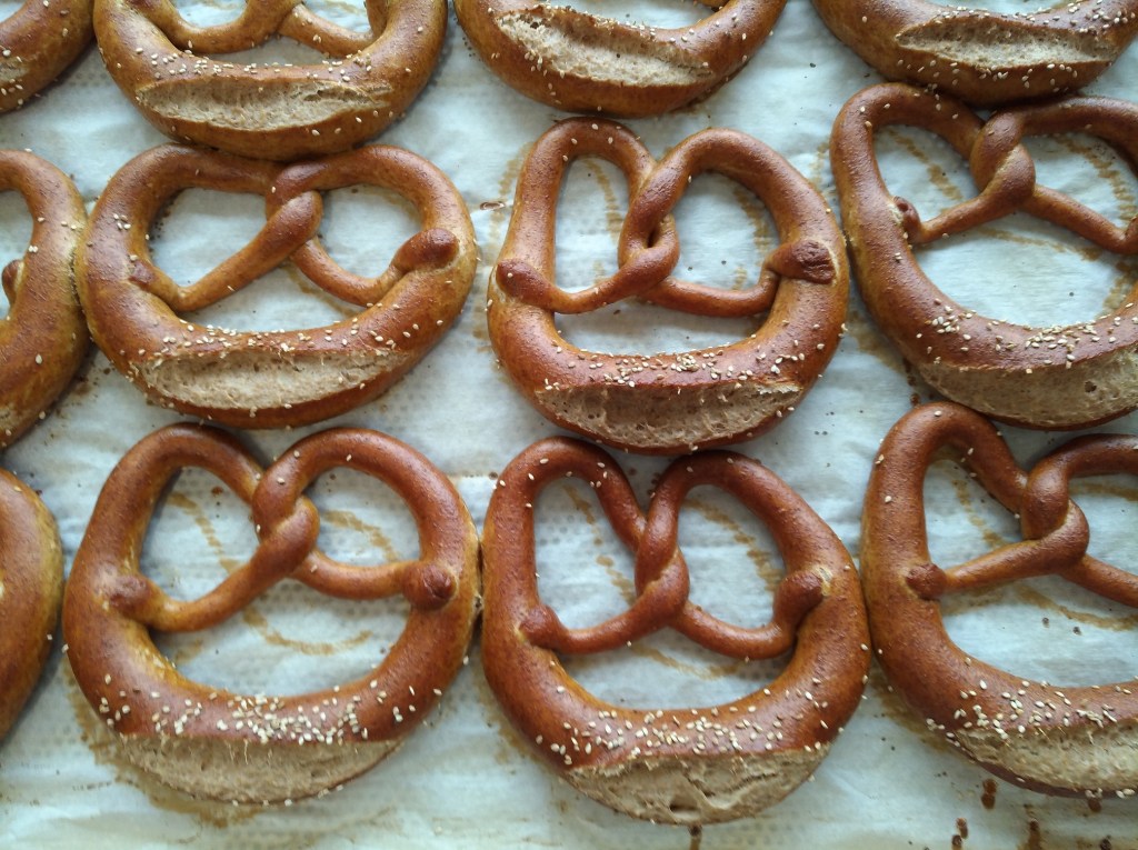 Brezeln aus Dinkelmehl mit einer goldbraunen Kruste und Sesam bestreut, angeordnet auf Backpapier.