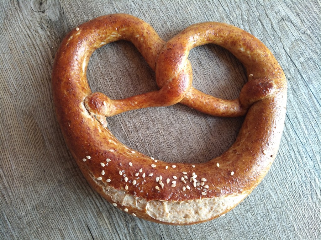 Ein frisch gebackenes, großes Laugenbrezel mit goldbrauner Kruste und Sesamkörnern, auf einem Holztisch.