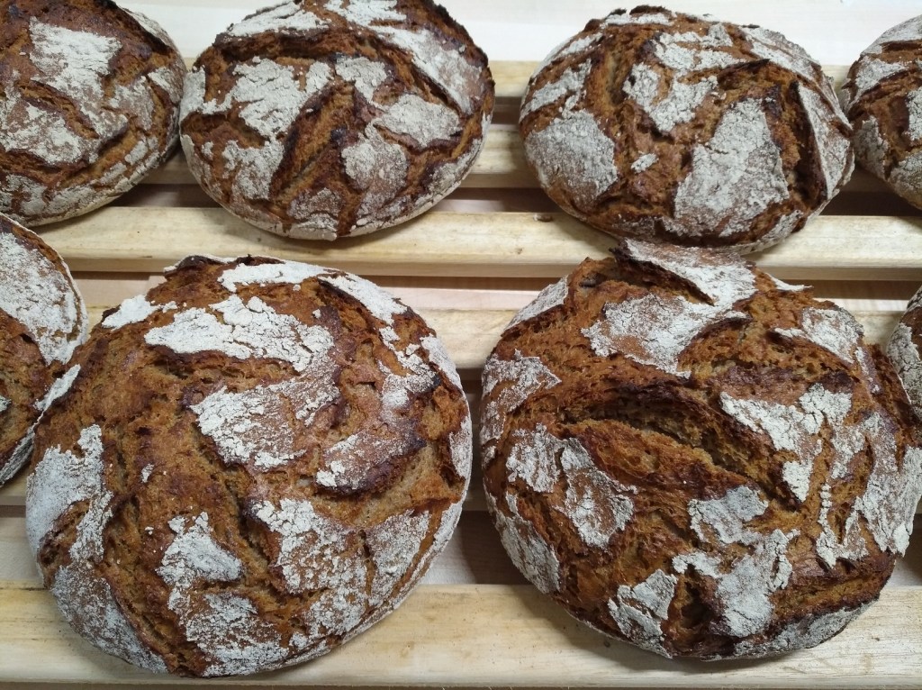 Rusticzne roggenowe chlebki na drewnianej tacy, z wyraźną fakturą i złotobrązową skórką.