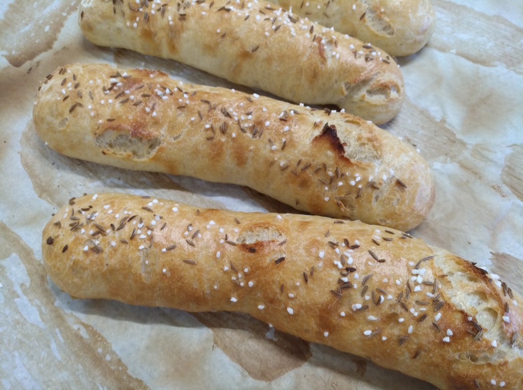 Drei frisch gebackene Brötchen mit Kümmel und Salz bestreut auf einem Backpapier.