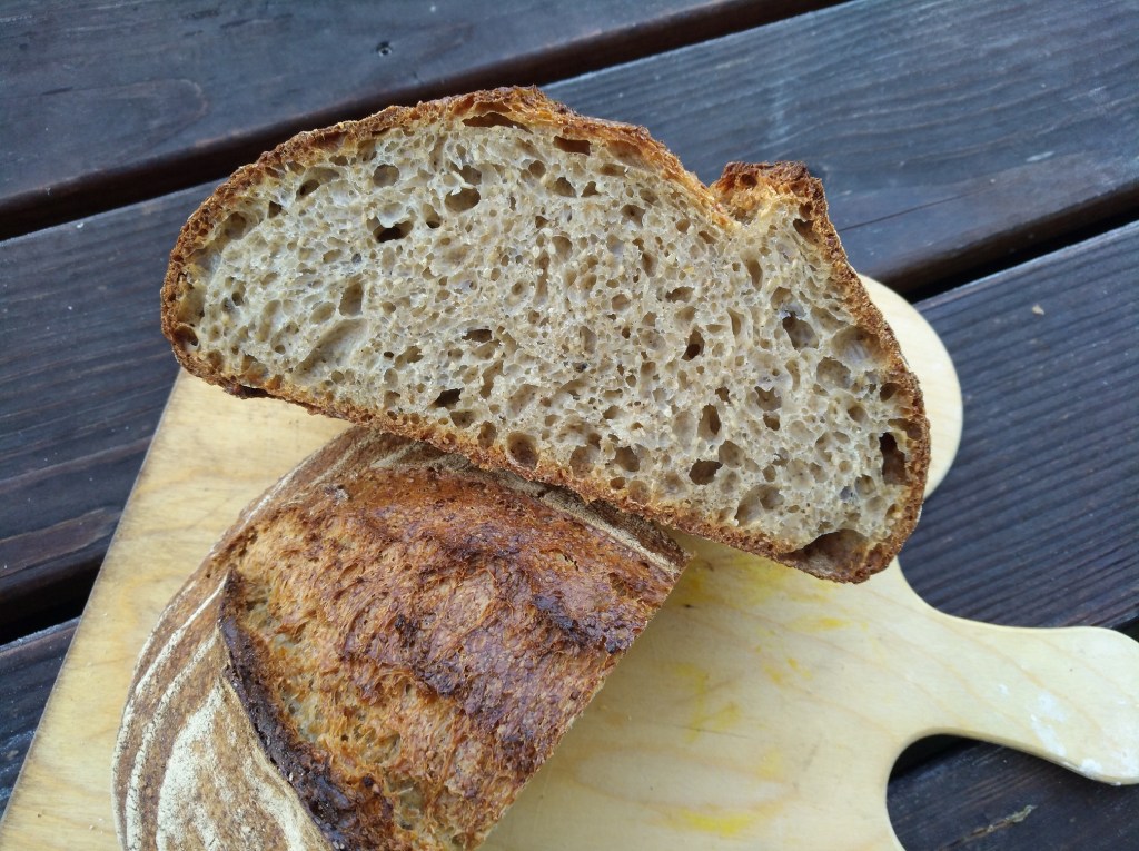 Eine aufgeschnittene Scheibe eines rustikalen Brotes mit knuspriger Kruste und heller, luftiger Krume, auf einem Holzbrett präsentiert.