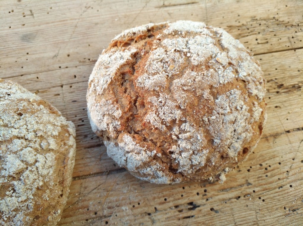Nahaufnahme von zwei rustikalen Brotlaiben auf einem Holzbrett, deren Oberfläche mit Mehl bestäubt ist.