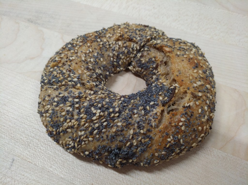 Ein Bagel mit einer Mischung aus Mohn- und Sesamsamen, auf einem Holzuntergrund platziert.