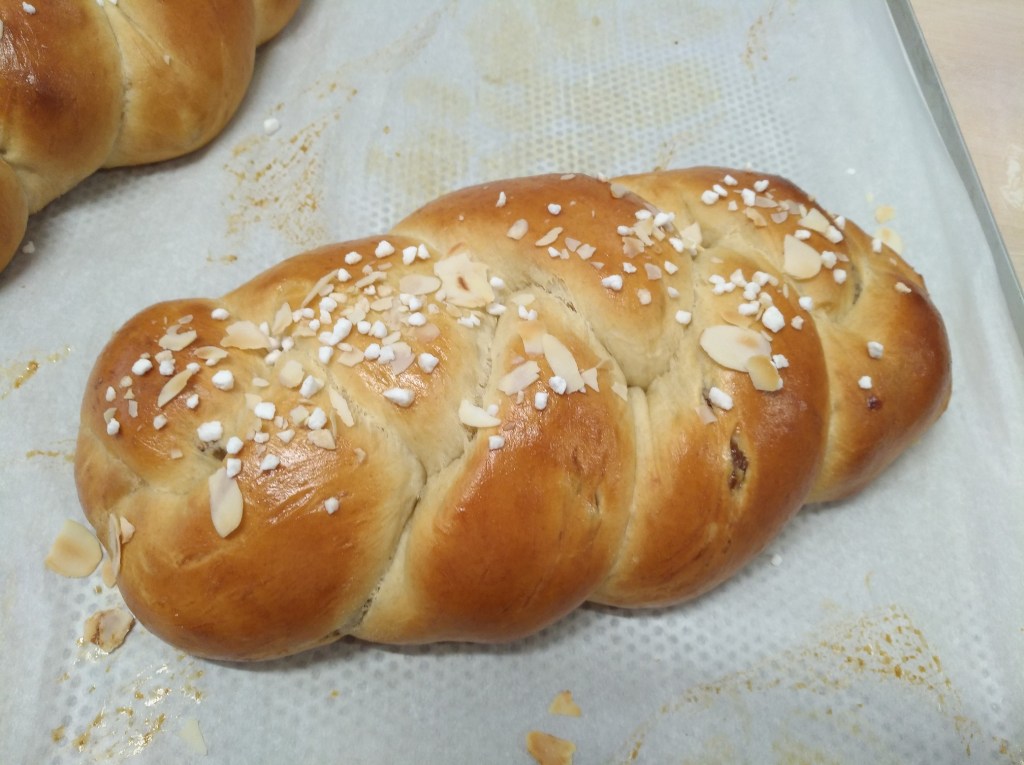 Ein frisch gebackener Hefezopf mit einer glänzenden Oberfläche und bestreut mit gehobelten Mandeln sowie Hagelzucker.