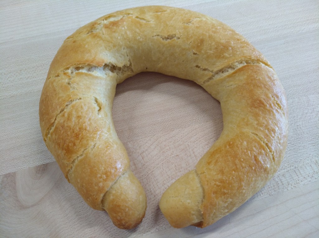 Ein frisch gebackenes, geschwungenes Brötchen auf einem Holzuntergrund.