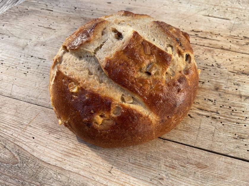 Ein runder Brotlaib mit einer goldbraunen Kruste, auf einer Holzoberfläche platziert.