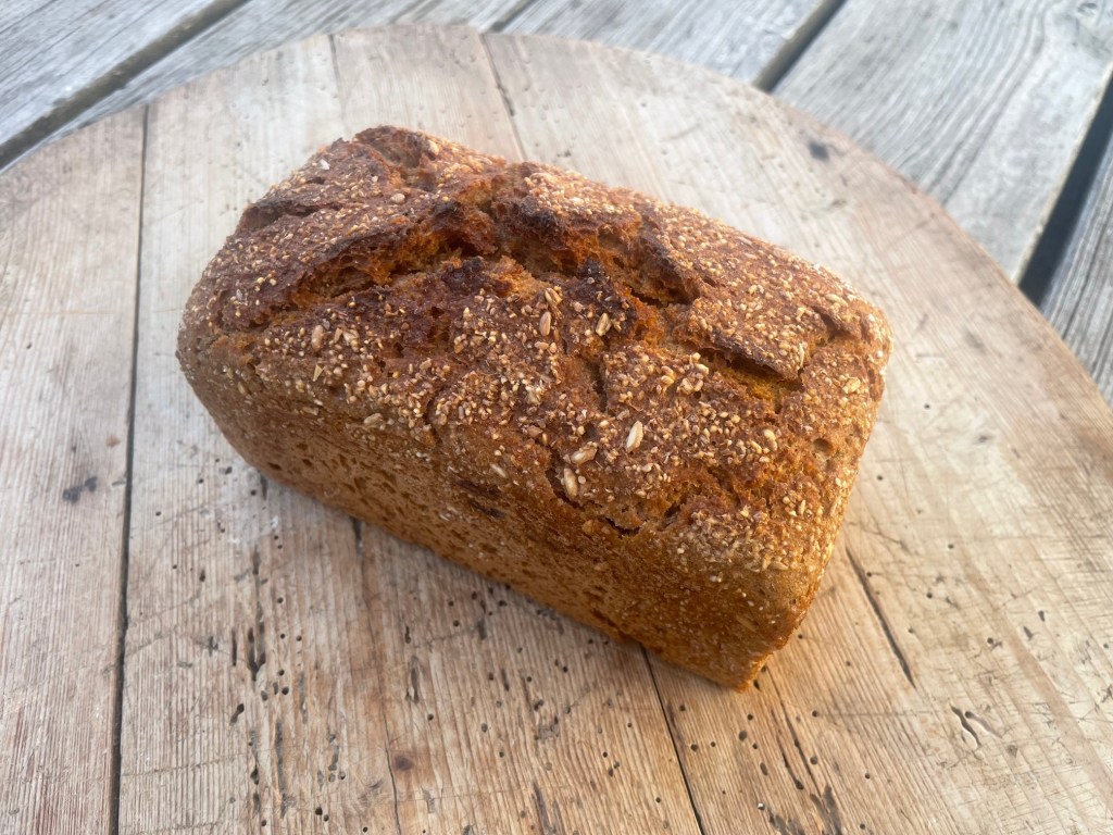 Ein frisch gebackenes Vollkornbrot mit einer rustikalen Kruste, auf einem Holztisch präsentiert.