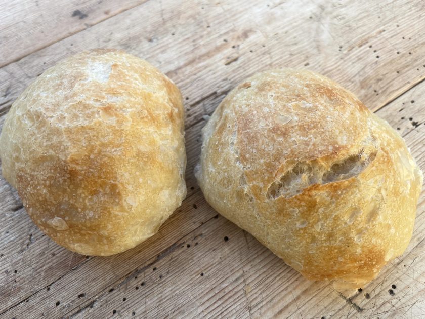 Zwei frisch gebackene Brötchen auf einer Holzoberfläche.